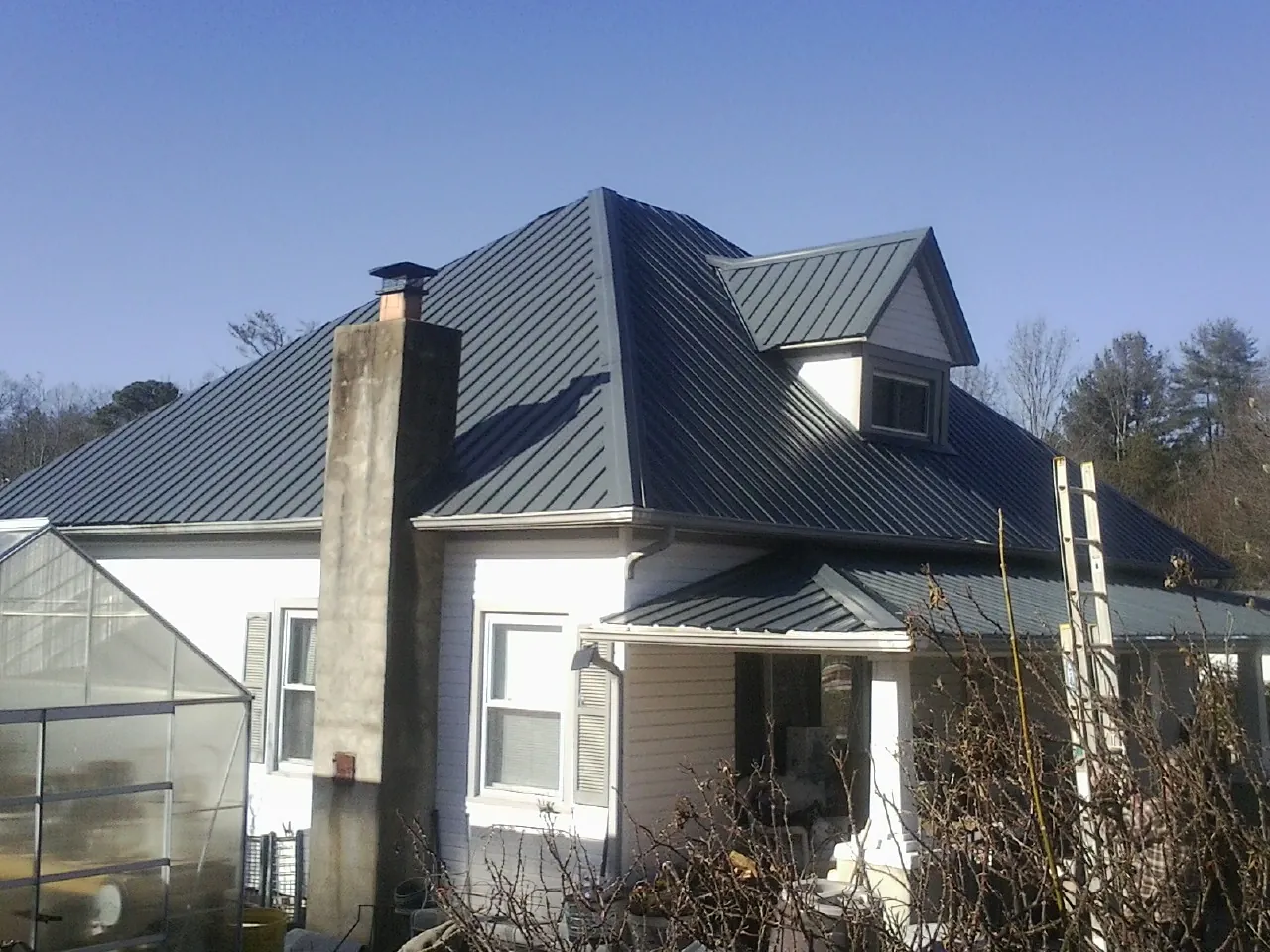 Dark blue standing seam metal roof on a white farmhouse with dormer — Slate & Tile Roof Repair by Roofing Brothers in Gilmer