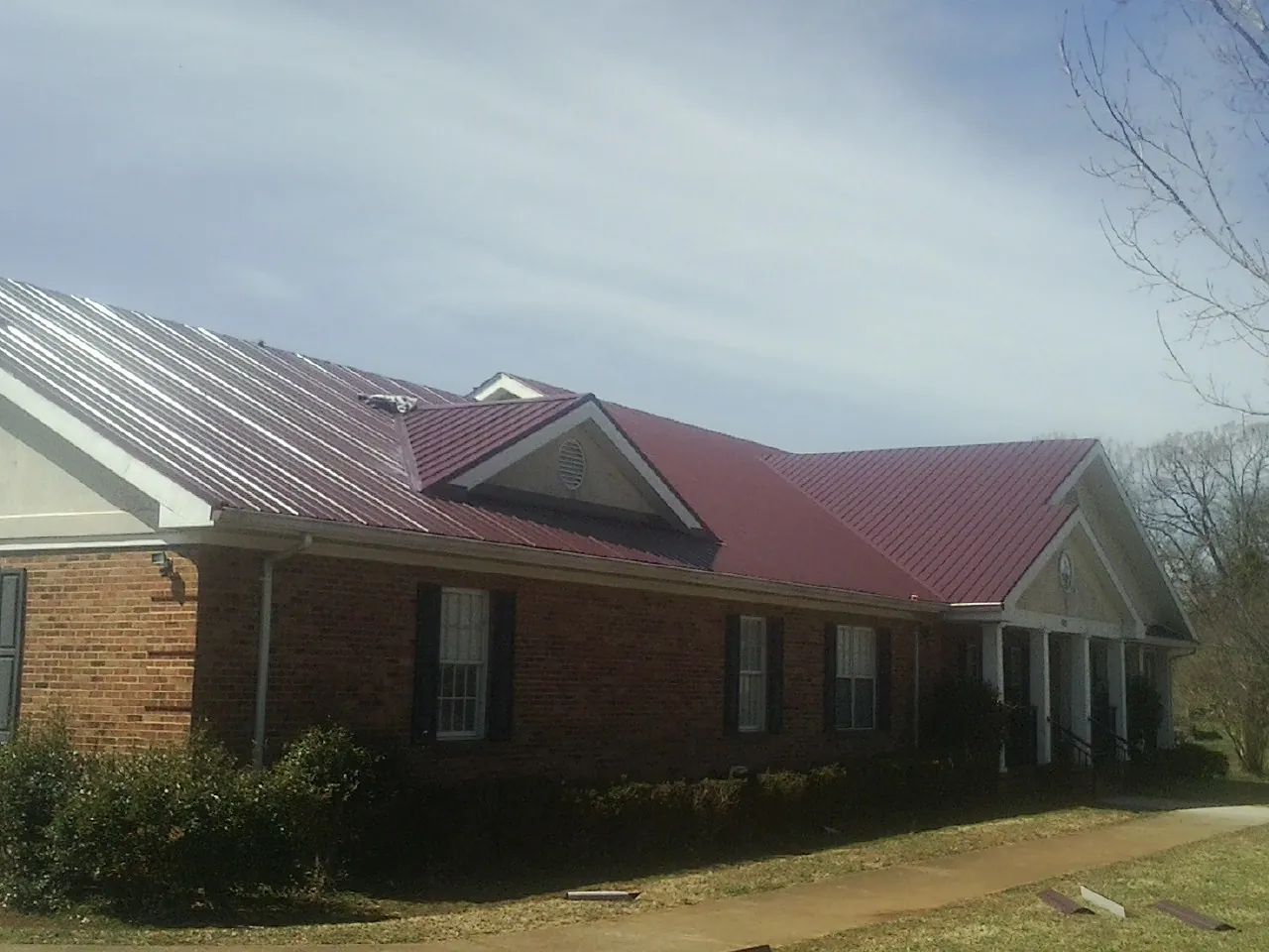 Red metal roof with gabled entries on a long brick building, from a Hail Damage Roof Repair job in Gilmer