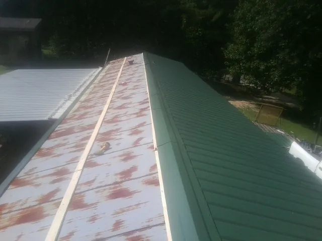 Old rusted panels beside newly installed green metal roofing — Wind Damage Roof Repair by Roofing Brothers in Gilmer