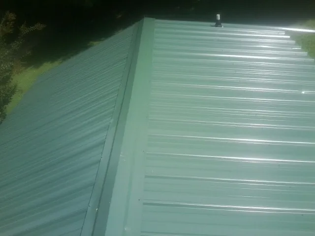 New green metal panels meeting at the ridge of a roof — Flat Roof Repair work by our crew in Gilmer