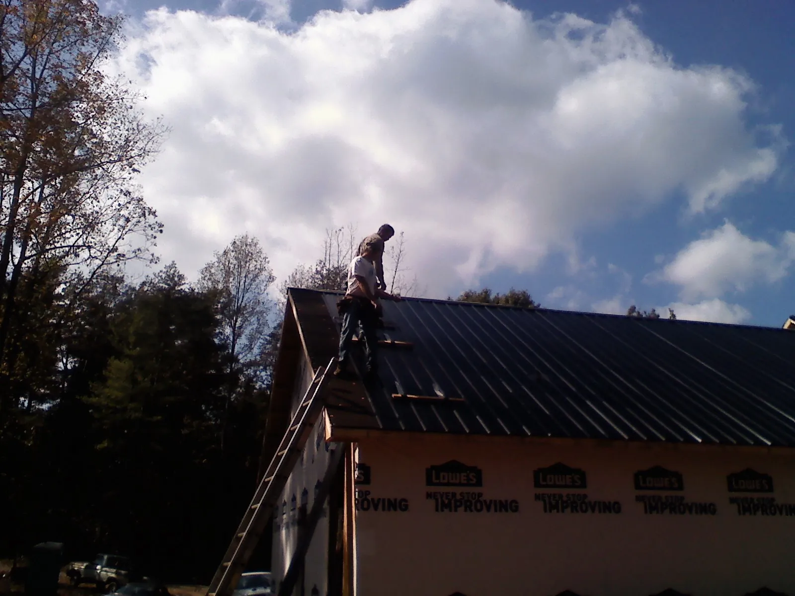 Roofer fastening dark metal panels high against a cloudy sky, from a Roof Inspection job in Gilmer