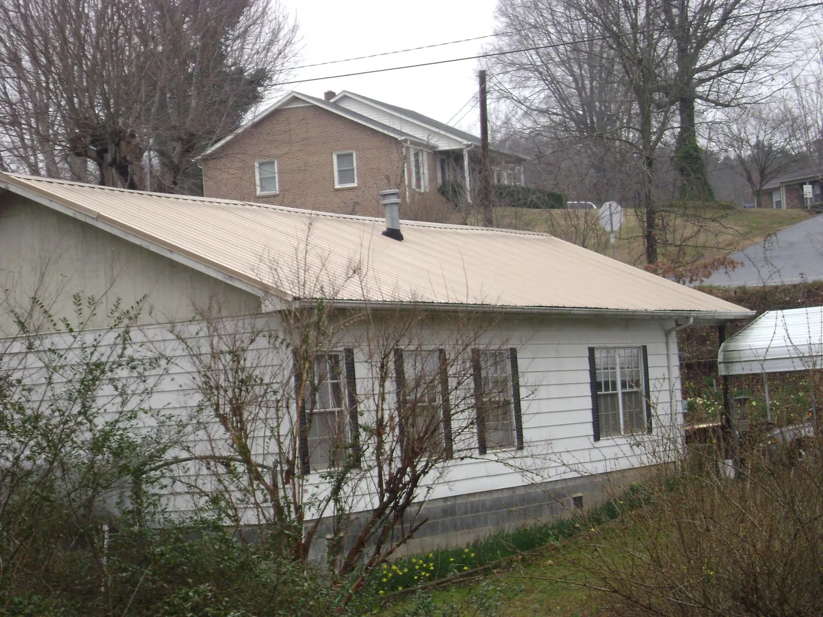 Tan metal roof on a white sided house set into a hillside — Commercial Roofing by Roofing Brothers in Gilmer
