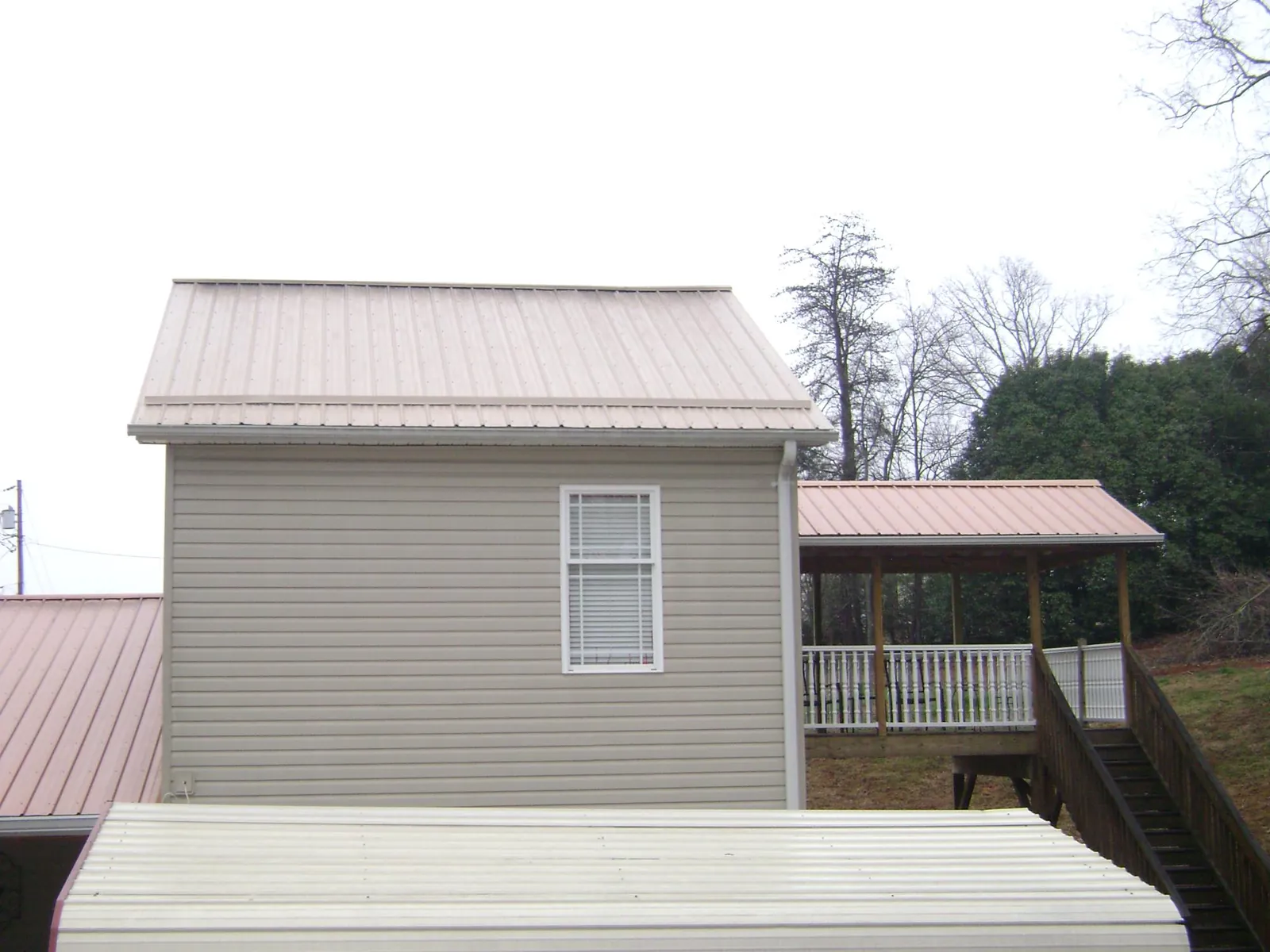 Tan metal roofs on a two story addition and attached porch, from a Roof Replacement job in Gilmer